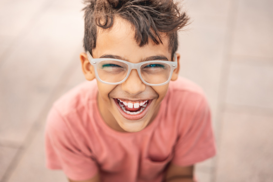 Brunette boy wearing glasses smiles with 28 adult teeth, an important dental milestone