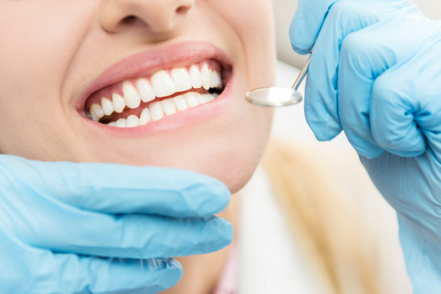 closeup of a woman's smile with blue gloved hands holding a special dental mirror during her routine dental exam