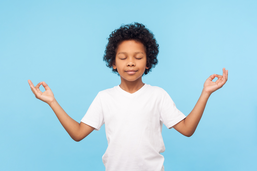 Black boy in a white t-shirt relaxes while holding a zen pose against a sky blue background